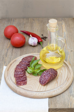 Salami sausage and sunflower oil in the bottles with herbs, tomatoes and spices on wooden table, selective focus