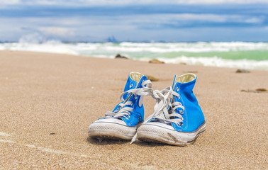 Obraz premium Blue pair of Worn sneakers on beach sand