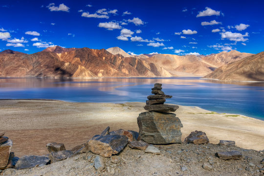 Fototapeta Rocks and reflection of Mountains on Pangong tso (Lake) with blue sky. It is huge lake in Ladakh, It is 134 km long and extends from India to Tibet. Leh, Ladakh, Jammu and Kashmir, India