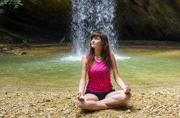 young caucasian female practicing yoga near the waterfall