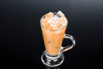 Refreshing ice cold tea with milk in transparent glass in dark backdrop