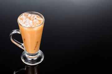 Refreshing ice cold tea with milk in transparent glass in dark backdrop