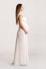 Fototapeta na wymiar Young and beautiful pregnant woman in antique dress over grey background with a lot of blank space