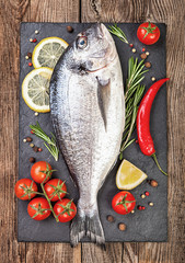 Fresh fish, lemon, spices and cherry tomatoes on a stone board