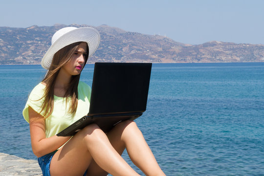 Young girl with laptop, in shorts and white hat outdoors.