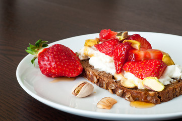 Dark rye bread topped with fresh strawberries, ricotta cheese and pistachio nuts and a drizzle of honey.