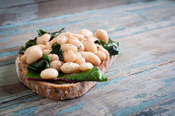 White cannellini beans, spinach and garlic on sourdough bread. A healthy vegetarian snack served on a rustic wood table.