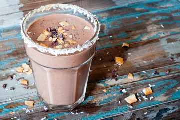 Chocolate coconut smoothie milkshake blended with cacau, coconut milk, banana and topped with coconut flakes and chia seeds. A healthy snack or treat served in a tall glass on a rustic wooden table.