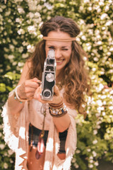 closeup on boho young woman among flowers using retro camera