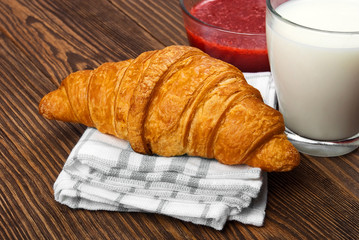 Croissants, milk and jam on old wooden table.