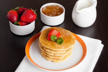 Delicious pancakes with fresh strawberries on a plate, jam and m