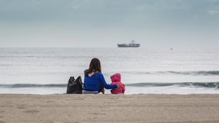 Little girl and young mom on beach watch ship