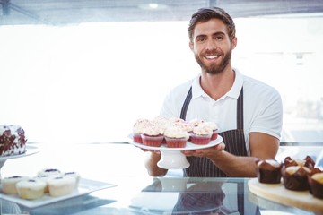  Smiling worker holding cupcakes behind the counter