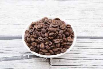 Roasted coffee beans in white bowl over rustic wooden background