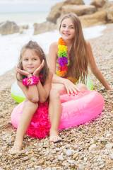 Two cute smiling girls are sitting on the beach