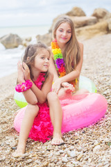 Two cute smiling girls are sitting on the beach