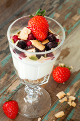 Homemade granola with Greek yoghurt topped with frozen berries, coconut and a fresh strawberry.Served in a tall glass.