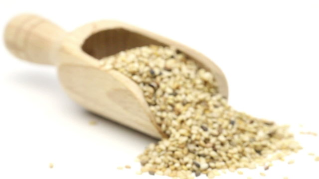 Dried organic sesame seeds in wooden scoop on white background focus shift