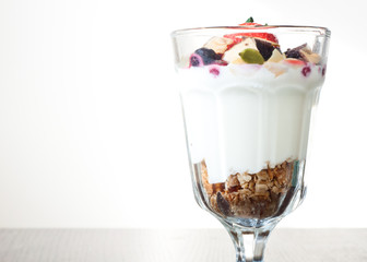 Homemade granola with Greek yoghurt topped with frozen berries, coconut and a fresh strawberry.Served in a tall glass.