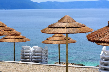Fototapeta premium Umbrellas on a beach with clear water and blue slippers