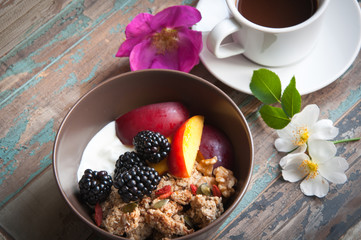 A bowl of healthy breakfast muesli with yogurt and topped with fresh blackberries, sliced nectarine, goji berries, pumpkin seeds and walnuts.Served with fresh coffee and wild flowers.