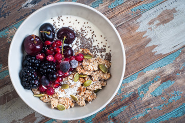 Healthy home made oatmeal porridge muesli with kefir yogurt and topped with blackberries, cherries,pomegranate, pumpkin and chia seeds. Served on a rustic wooden table.