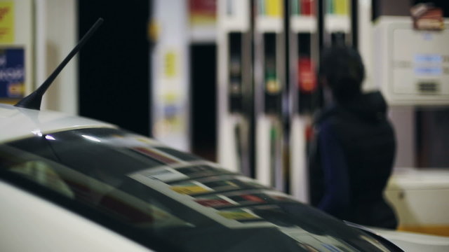 Woman refueling car at gas station pump at night