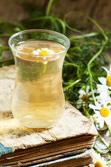 cup of black tea, wild chamomile, old books on wood background,