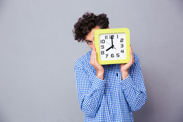 Man covering face with clock and looking at camera