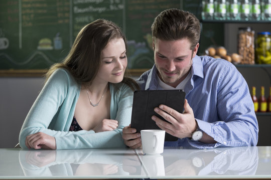 A Young Couple Using A Tablet/ipad In A Cafe