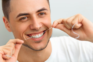 Closeup of young man flossing his teeth. Cleaning teeth with den