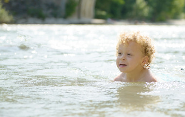 portrait of a young blonde boy playing in water