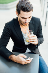 Young italian boy drinking while checking is smartphone