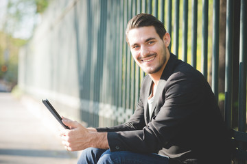 Fototapeta premium Young italian boy seated on a sidewalk using tablet