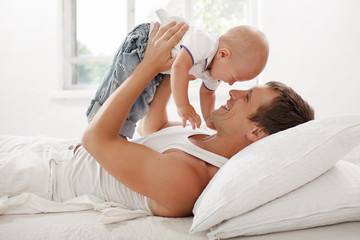 young father with his nine months old som on the bed at home