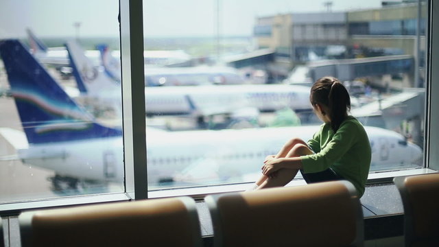 Child at the airport near the window looking at airplanes and waiting for time of flight