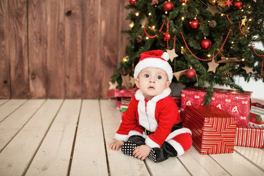 Baby in santa suit with gifts near xmas tree