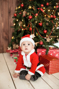 Baby in santa suit with gifts near xmas tree