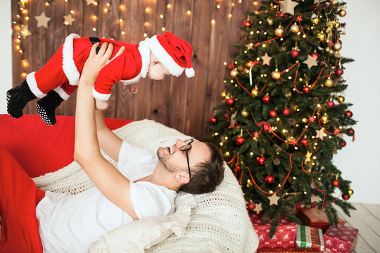Hipster father holding baby in santa suit in the air