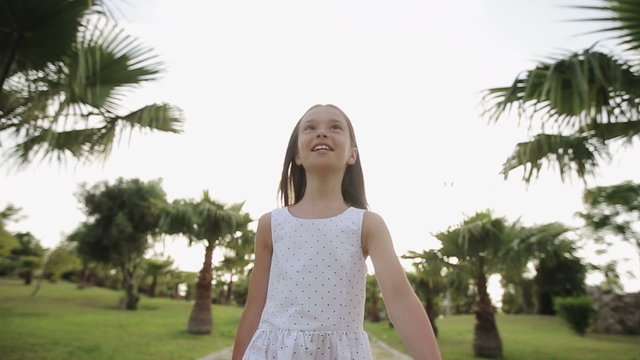 Child walks through a palm alley at sunset, rejoices and sings