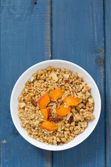 granola with fruits and nuts in white bowl on blue wooden background