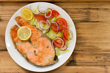 Fototapeta na wymiar fried salmon with vegetable salad and lemon on plate on brown ooden background