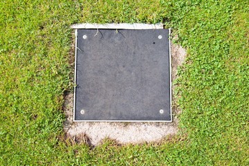 Metal manhole cover drainage system in the midst of cropped grass