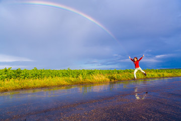 Girl jumping on wet road with rainbow