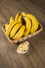 A banch of bananas and a sliced banana in a pot over a table.