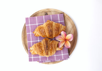 Fototapeta na wymiar Golden brown croissant and plulmeria flower on wooden plate