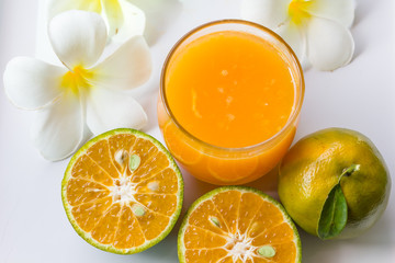 orange juice in a glass decorated with half fresh orange and flower on white background
