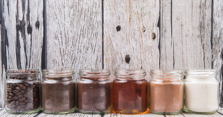 Coffee beans, coffee powder, creamer, cocoa powder, honey and processed tea leaves in a mason jar over weathered wooden background