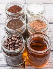 Coffee beans, coffee powder, creamer, cocoa powder, honey and processed tea leaves in a mason jar over weathered wooden background