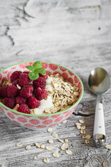 oatmeal with raspberries and natural yoghurt in a bowl on a light wooden background